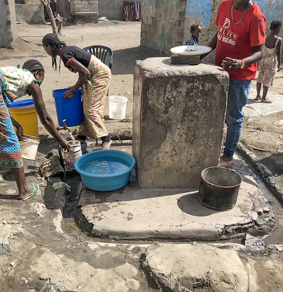 20〜30世帯で共有する屋外の水道水栓で水を汲む様子。水圧が低いため、蛇口は地面スレスレにある。汲んだ水は家で溜められるが飲むまでに汚染がすすむ。